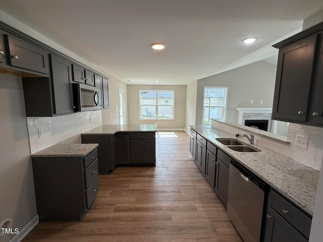 kitchen with light stone counters, kitchen peninsula, wood-type flooring, backsplash, and appliances with stainless steel finishes