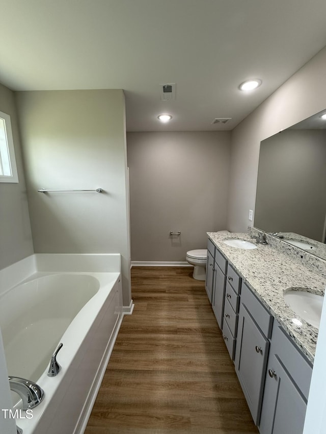 bathroom featuring vanity, a tub to relax in, hardwood / wood-style floors, and toilet