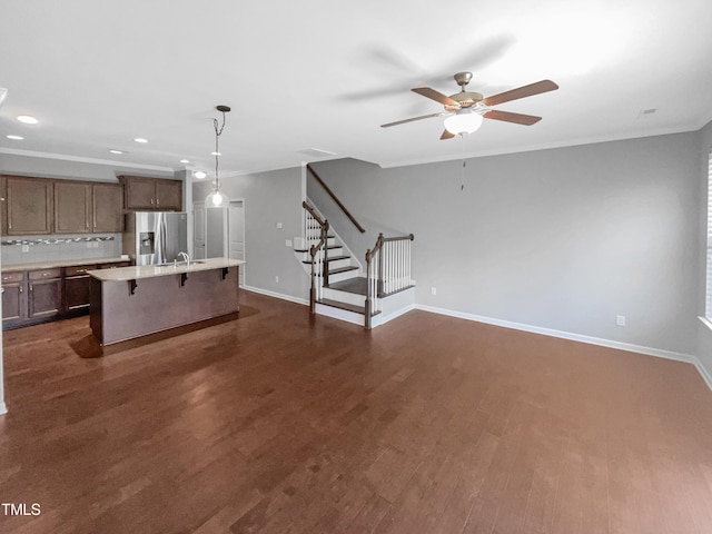 kitchen with stainless steel refrigerator with ice dispenser, dark wood-type flooring, a breakfast bar area, hanging light fixtures, and an island with sink