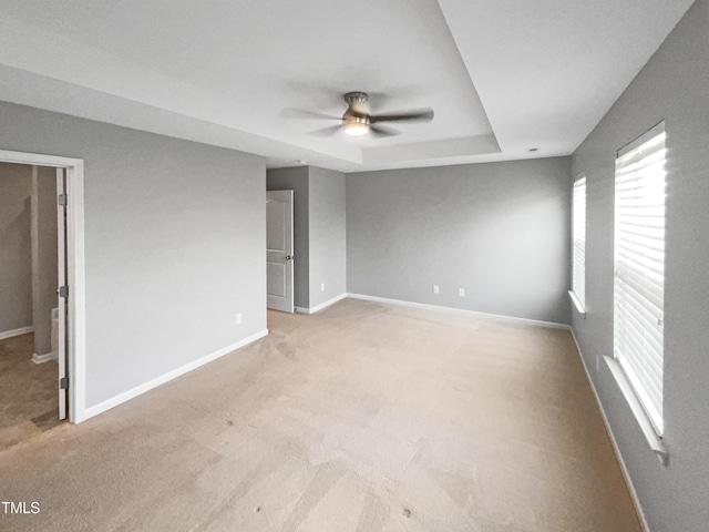 unfurnished room featuring ceiling fan, a raised ceiling, and light colored carpet