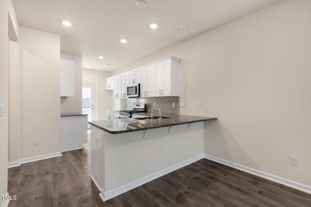 kitchen featuring dark hardwood / wood-style floors, kitchen peninsula, appliances with stainless steel finishes, white cabinets, and dark stone counters