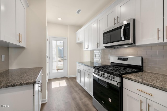 kitchen with white cabinets, stainless steel appliances, dark stone countertops, decorative backsplash, and light hardwood / wood-style flooring