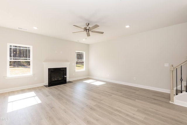 unfurnished living room with light wood finished floors, visible vents, a ceiling fan, a fireplace with flush hearth, and stairs