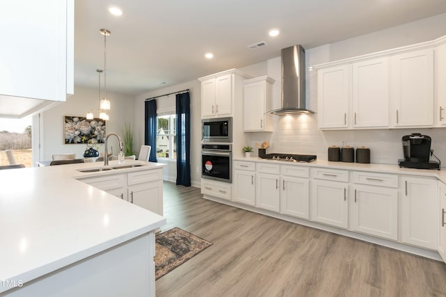 kitchen with a sink, wall chimney exhaust hood, appliances with stainless steel finishes, and light countertops