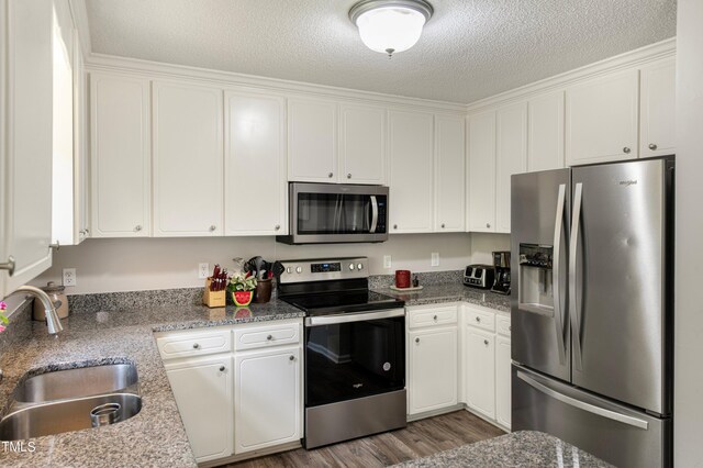 kitchen with appliances with stainless steel finishes, dark hardwood / wood-style floors, sink, white cabinets, and a textured ceiling