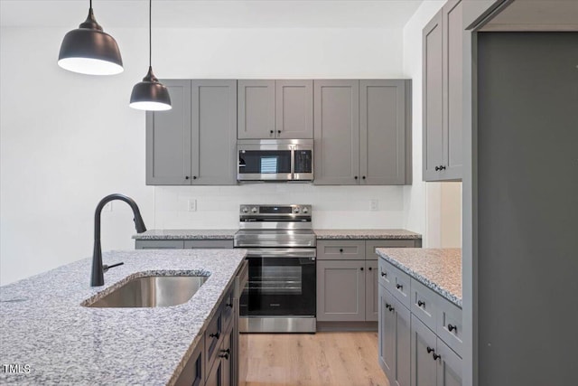 kitchen with stainless steel appliances, sink, pendant lighting, and light stone counters