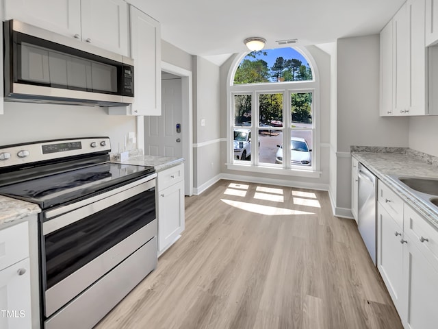 kitchen with white cabinets, stainless steel appliances, baseboards, and light wood-style floors