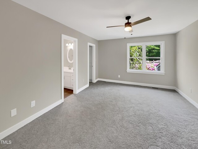 empty room with a sink, ceiling fan, carpet floors, baseboards, and visible vents