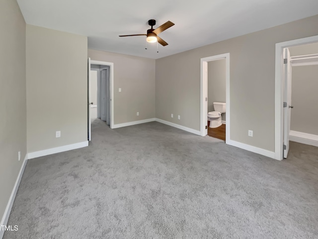 unfurnished bedroom with ensuite bath, carpet, a spacious closet, and baseboards