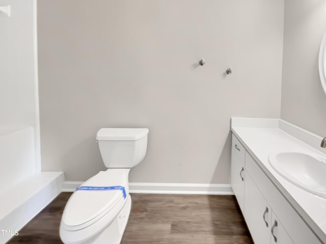 bathroom featuring baseboards, wood finished floors, toilet, and vanity