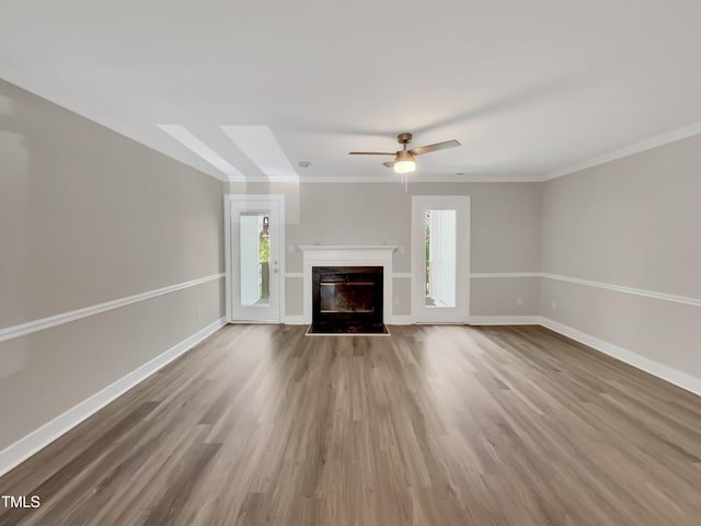 unfurnished living room featuring plenty of natural light, wood finished floors, a glass covered fireplace, and baseboards