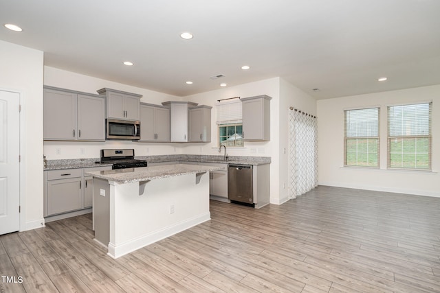 kitchen featuring light hardwood / wood-style floors, light stone counters, a kitchen breakfast bar, a kitchen island, and appliances with stainless steel finishes