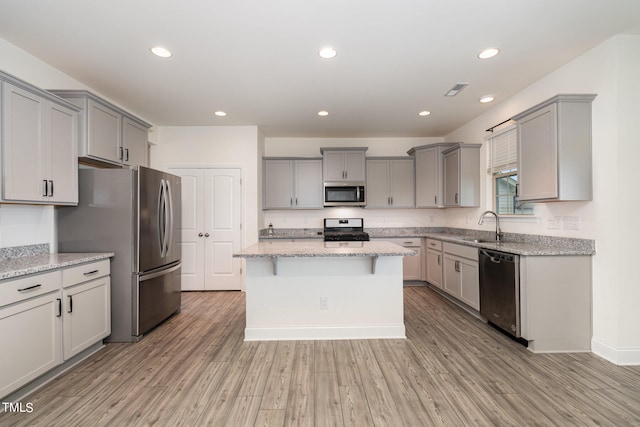 kitchen with gray cabinetry, a center island, appliances with stainless steel finishes, light stone countertops, and light hardwood / wood-style flooring