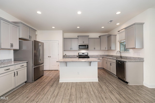 kitchen featuring light stone counters, stainless steel appliances, gray cabinets, and a kitchen island