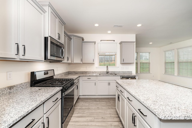 kitchen featuring light stone counters, appliances with stainless steel finishes, sink, and light hardwood / wood-style flooring