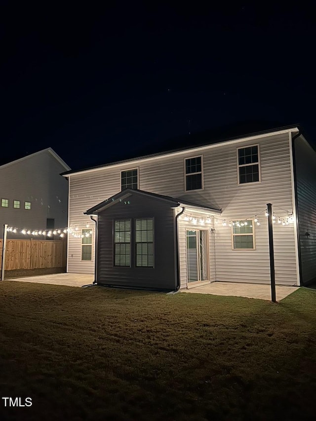 back house at night featuring a lawn and a patio