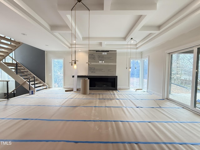 unfurnished living room with beam ceiling, coffered ceiling, stairway, and baseboards