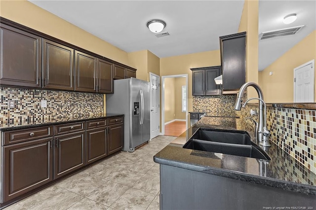 kitchen with stainless steel fridge, sink, dark brown cabinets, backsplash, and dark stone counters