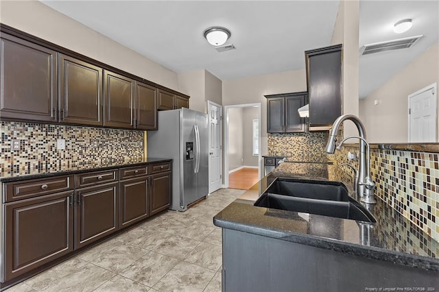 kitchen with tasteful backsplash, dark brown cabinetry, dark stone countertops, sink, and stainless steel fridge with ice dispenser