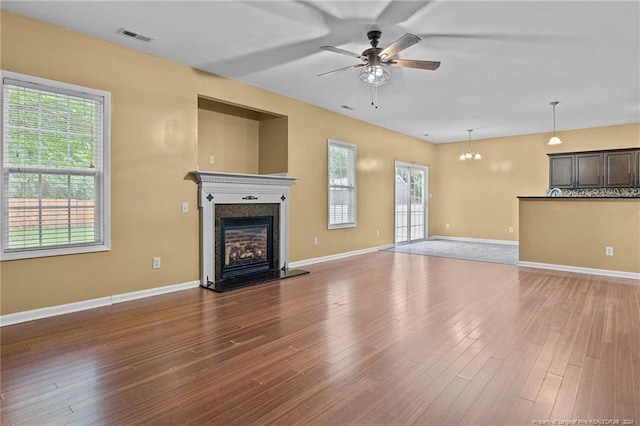 unfurnished living room featuring ceiling fan with notable chandelier, a healthy amount of sunlight, and dark wood-type flooring