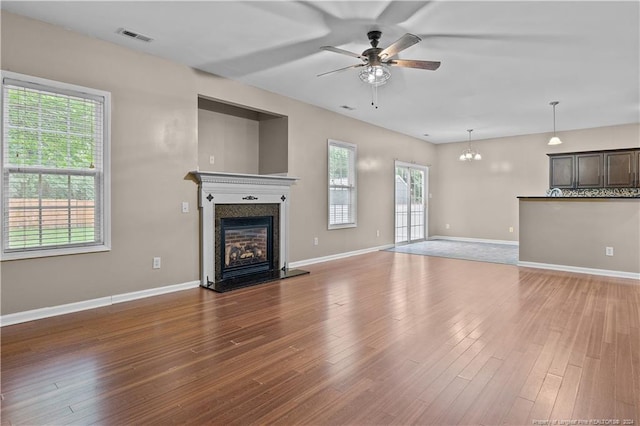 unfurnished living room with ceiling fan with notable chandelier, hardwood / wood-style floors, and a healthy amount of sunlight