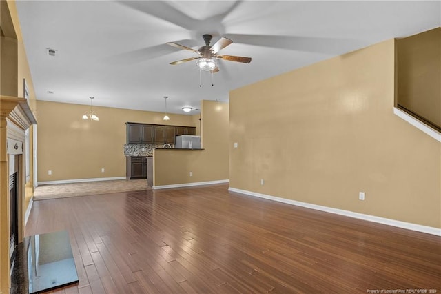 unfurnished living room with ceiling fan with notable chandelier and dark wood-type flooring