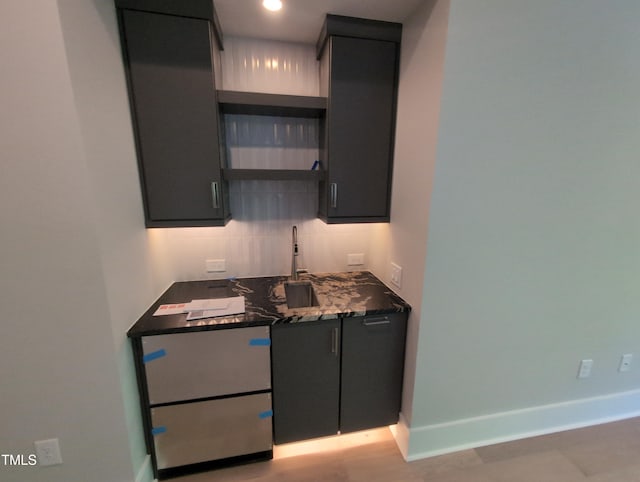 kitchen with backsplash, dark cabinets, and dark stone countertops