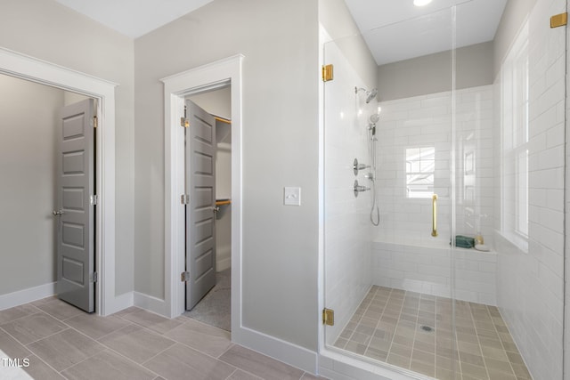 full bathroom with a spacious closet, a shower stall, and baseboards