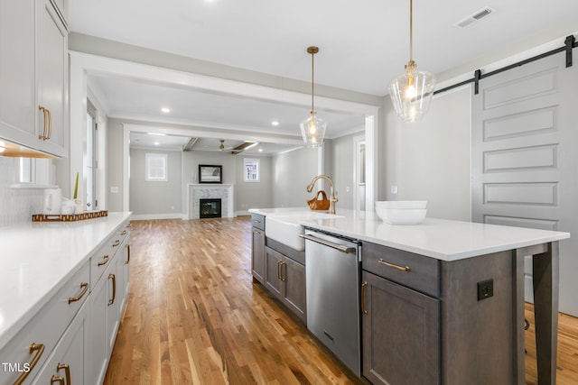 kitchen with stainless steel dishwasher, a barn door, light wood-style floors, light countertops, and a sink