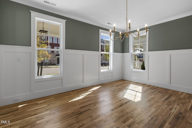 unfurnished dining area with a notable chandelier, wood-type flooring, and ornamental molding