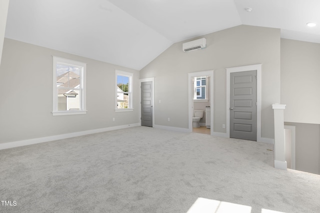 unfurnished bedroom featuring an AC wall unit, ensuite bathroom, vaulted ceiling, and light carpet