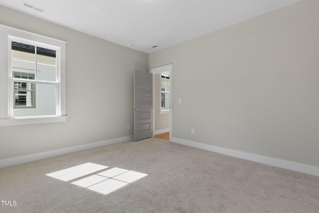 spare room featuring carpet flooring, baseboards, a wealth of natural light, and visible vents