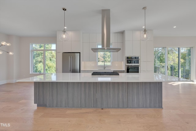 kitchen featuring decorative light fixtures, light hardwood / wood-style flooring, island exhaust hood, stainless steel appliances, and a large island