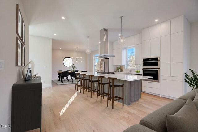 kitchen featuring a spacious island, decorative light fixtures, white cabinets, and island exhaust hood