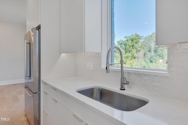 kitchen with light stone countertops, light hardwood / wood-style flooring, sink, high quality fridge, and white cabinets