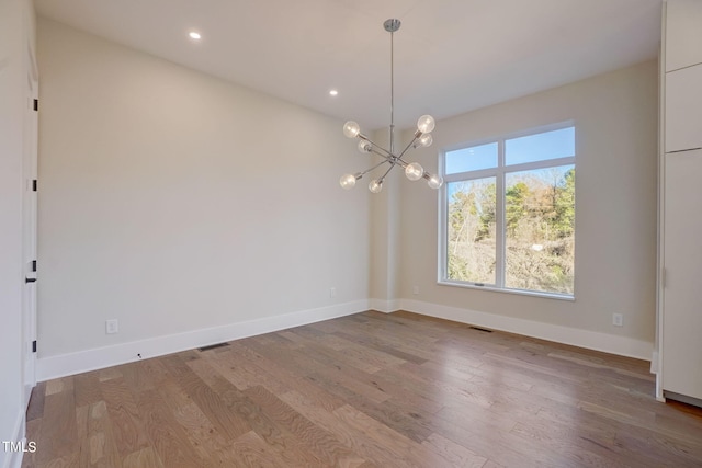 unfurnished room featuring wood-type flooring and an inviting chandelier