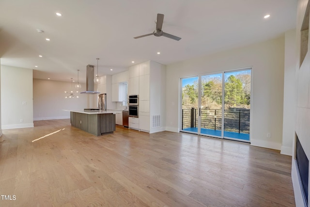 unfurnished living room with ceiling fan with notable chandelier and light hardwood / wood-style floors