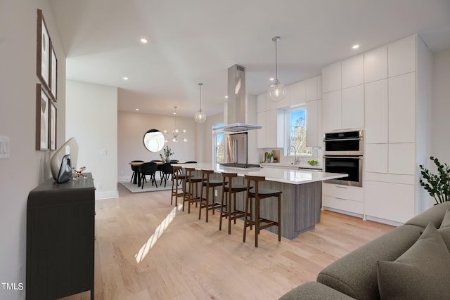 kitchen featuring pendant lighting, a large island, white cabinets, and island range hood