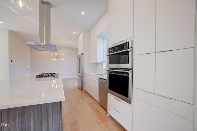 kitchen featuring light wood-type flooring, white cabinetry, stainless steel appliances, an inviting chandelier, and island exhaust hood