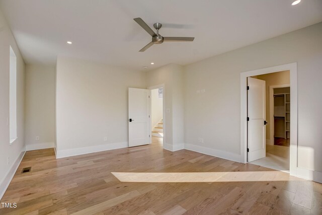 unfurnished bedroom featuring light wood-type flooring, a walk in closet, and ceiling fan