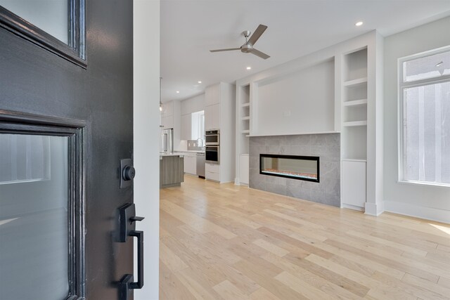 living room featuring a fireplace, light hardwood / wood-style flooring, built in shelves, and ceiling fan