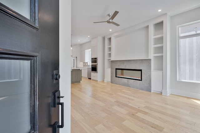 living room with built in features, plenty of natural light, a tile fireplace, and light hardwood / wood-style floors