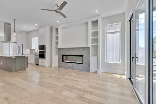 unfurnished living room featuring plenty of natural light, ceiling fan, and light hardwood / wood-style floors