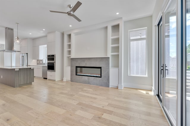 unfurnished living room with built in shelves, sink, light wood-type flooring, ceiling fan, and a tiled fireplace