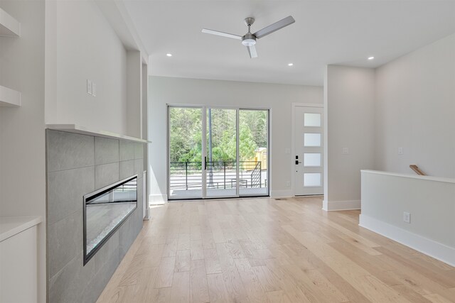 unfurnished living room with ceiling fan, a tile fireplace, and light hardwood / wood-style floors