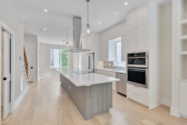 kitchen featuring white cabinetry, island range hood, a center island, hanging light fixtures, and appliances with stainless steel finishes