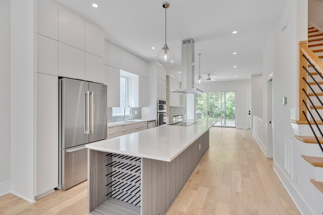 kitchen featuring white cabinets, light wood-type flooring, decorative light fixtures, stainless steel appliances, and a center island with sink