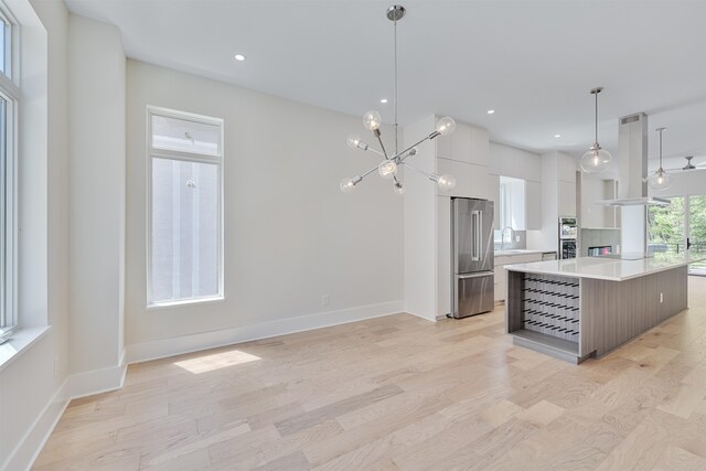 kitchen featuring a kitchen island, hanging light fixtures, stainless steel appliances, white cabinetry, and light wood-type flooring