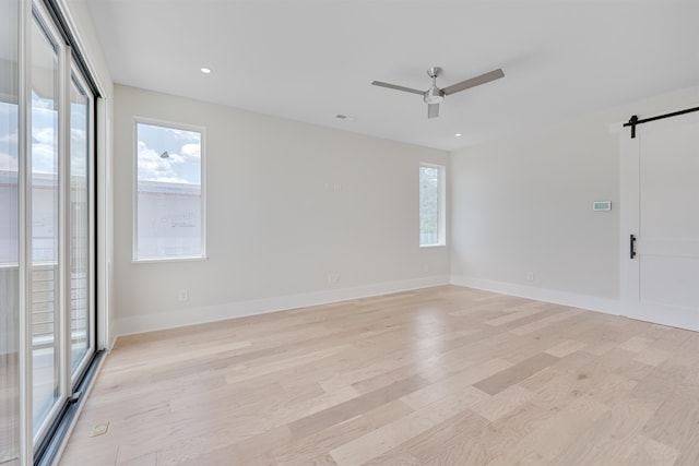 empty room featuring light wood-type flooring, ceiling fan, and a barn door