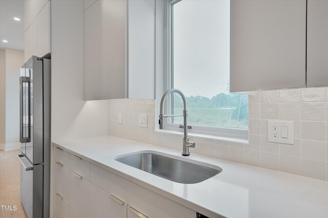 kitchen featuring backsplash, light hardwood / wood-style flooring, white cabinetry, sink, and stainless steel fridge